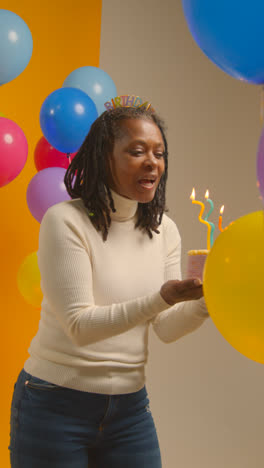 Vertical-Video-Studio-Shot-Of-Woman-Wearing-Birthday-Headband-Celebrating-Birthday-Blowing-Out-Candles-On-Cake-1